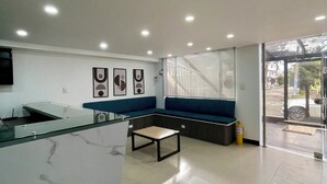 A modern reception area with a marble counter, a seating area with blue cushions, and a glass door leading outside. - Hotel Embajada 44 (Bogotá)