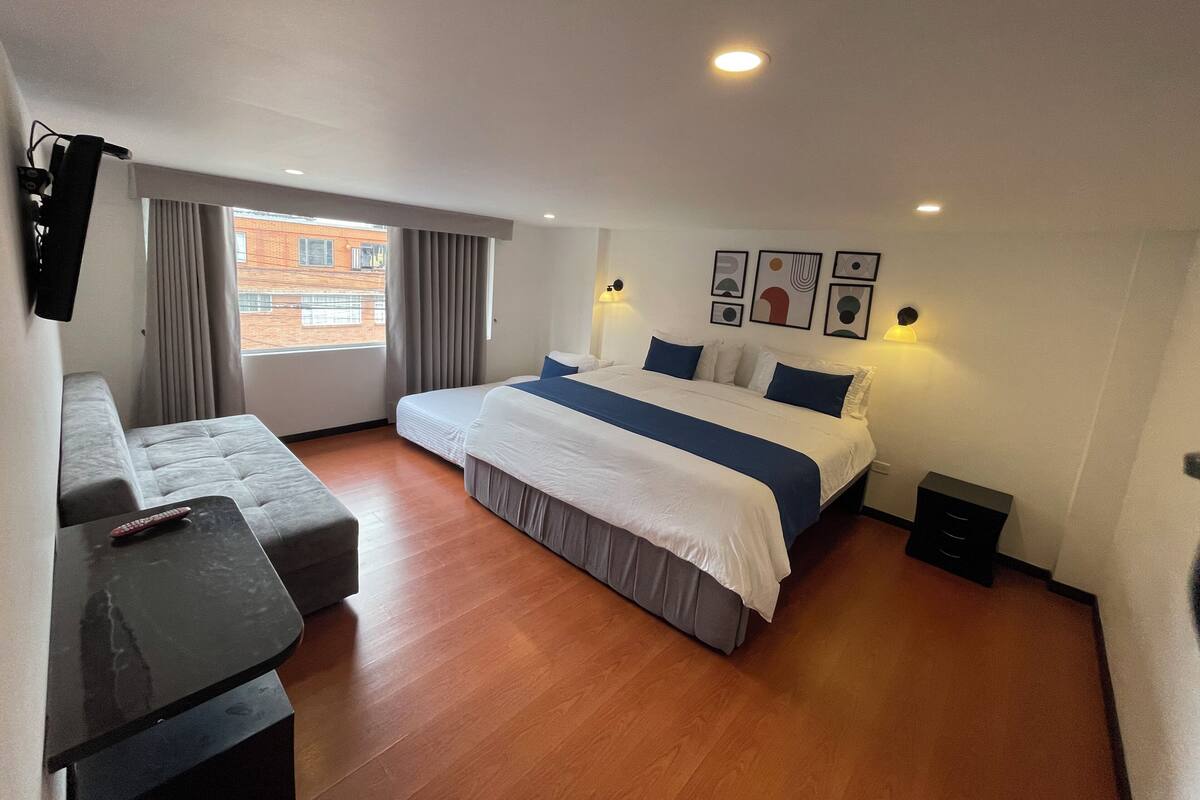 Ein modernes Hotelzimmer mit einem großen Bett, einer Couch, einem kleinen Tisch und einem Fenster mit Vorhängen.