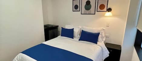 A bedroom with a large bed, white walls, and a ceiling light.