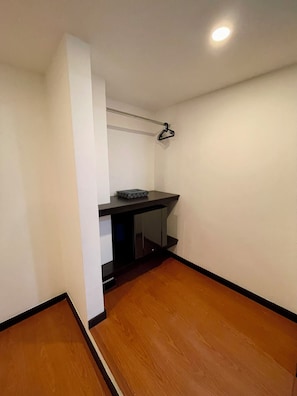 A small, narrow room with a wooden floor, a black desk, and a hanging clothes rack. - Hotel Embajada 44 (Bogotá)