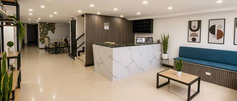 Un vestíbulo de hotel con una recepción, una zona de estar y una escalera.