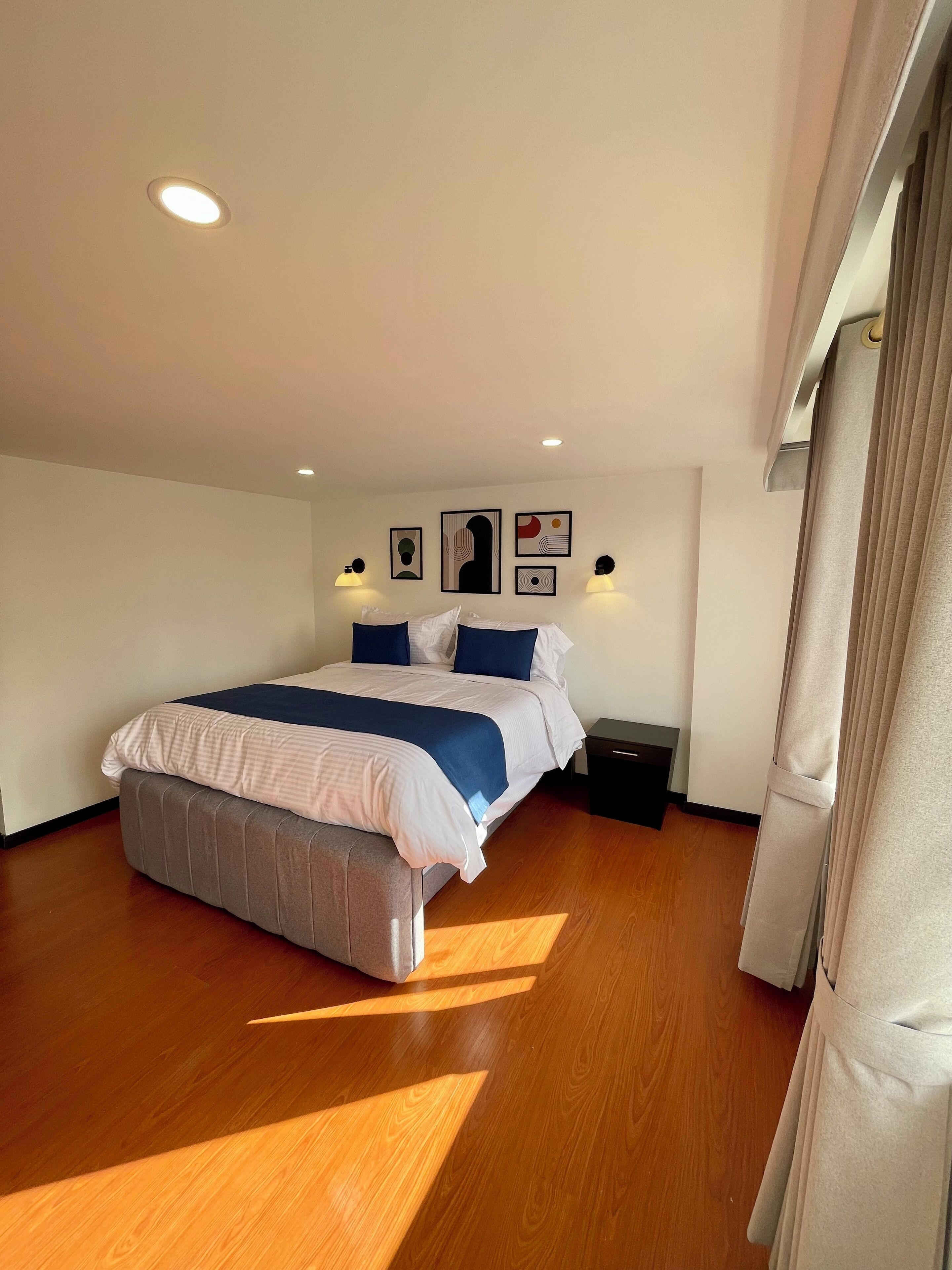 Una habitación de hotel moderna con una cama grande, suelo de madera y una lámpara de techo.