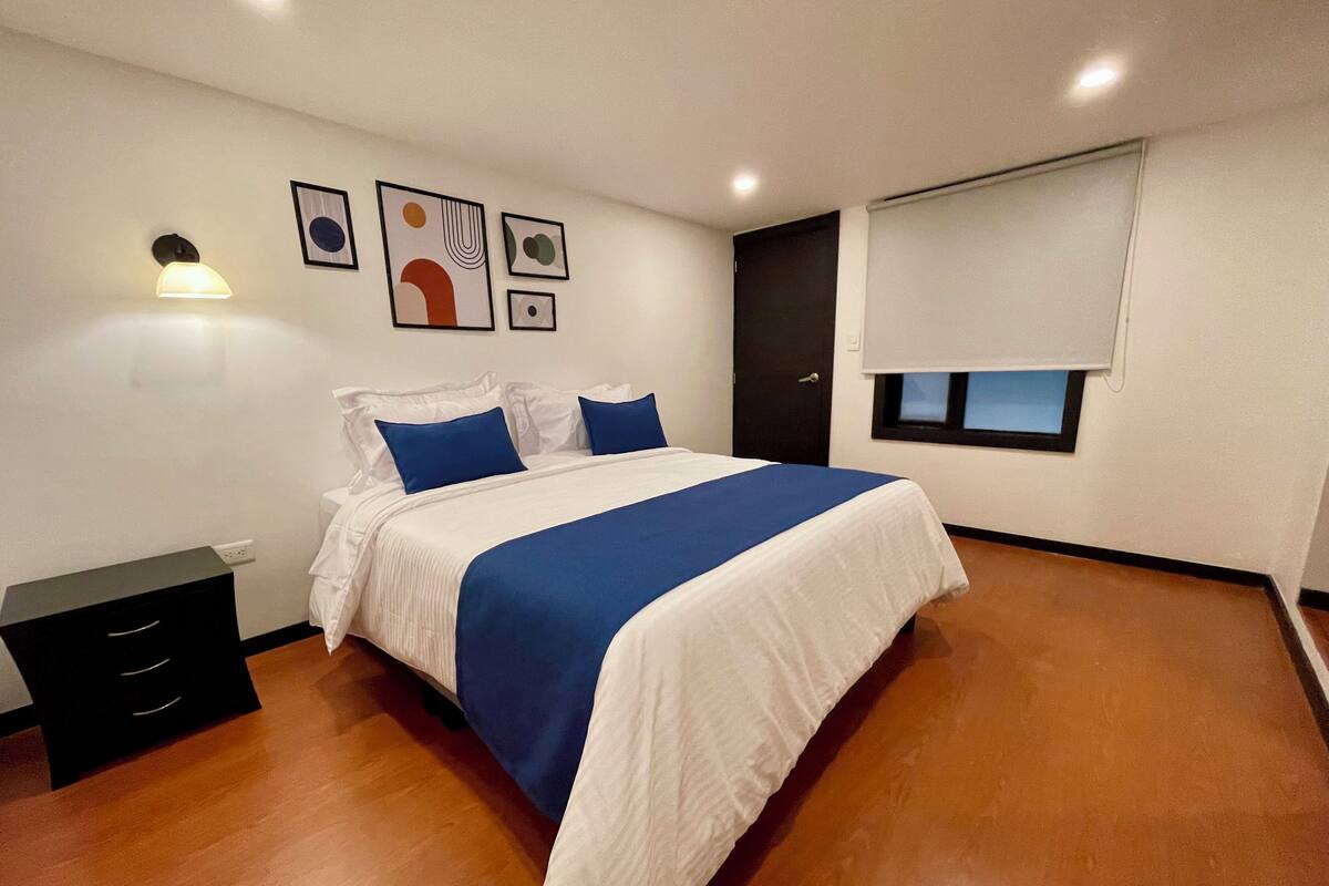 Ein Schlafzimmer mit einem Bett, einem Nachttisch, einer Wandleuchte und Kunstwerken.