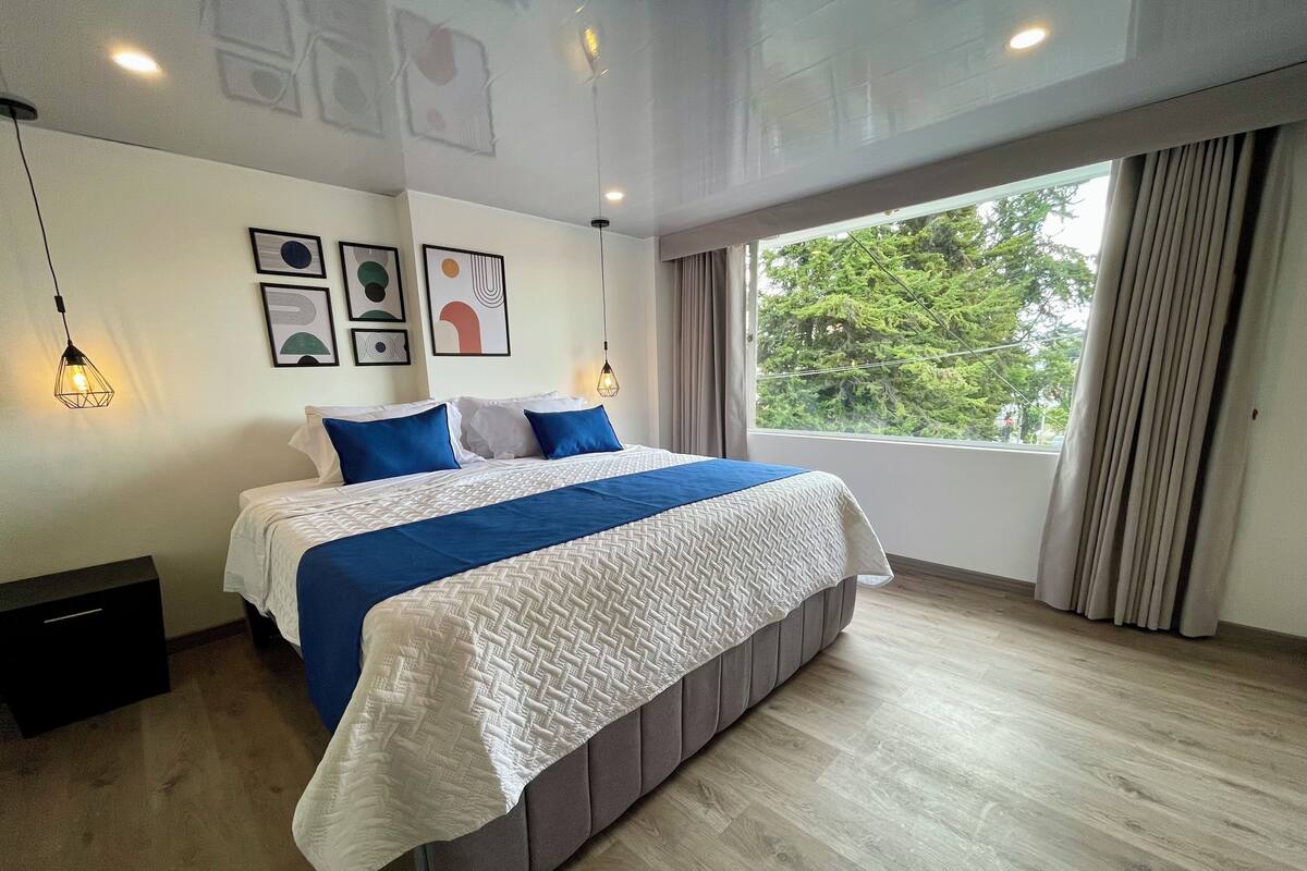 Ein modernes Schlafzimmer mit einem großen Bett, einem Fenster mit Vorhängen und Kunstwerken an der Wand.