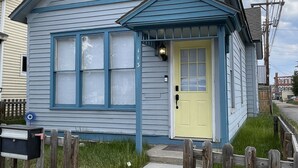 A small, single-story house with a yellow front door, blue trim, and a small porch.