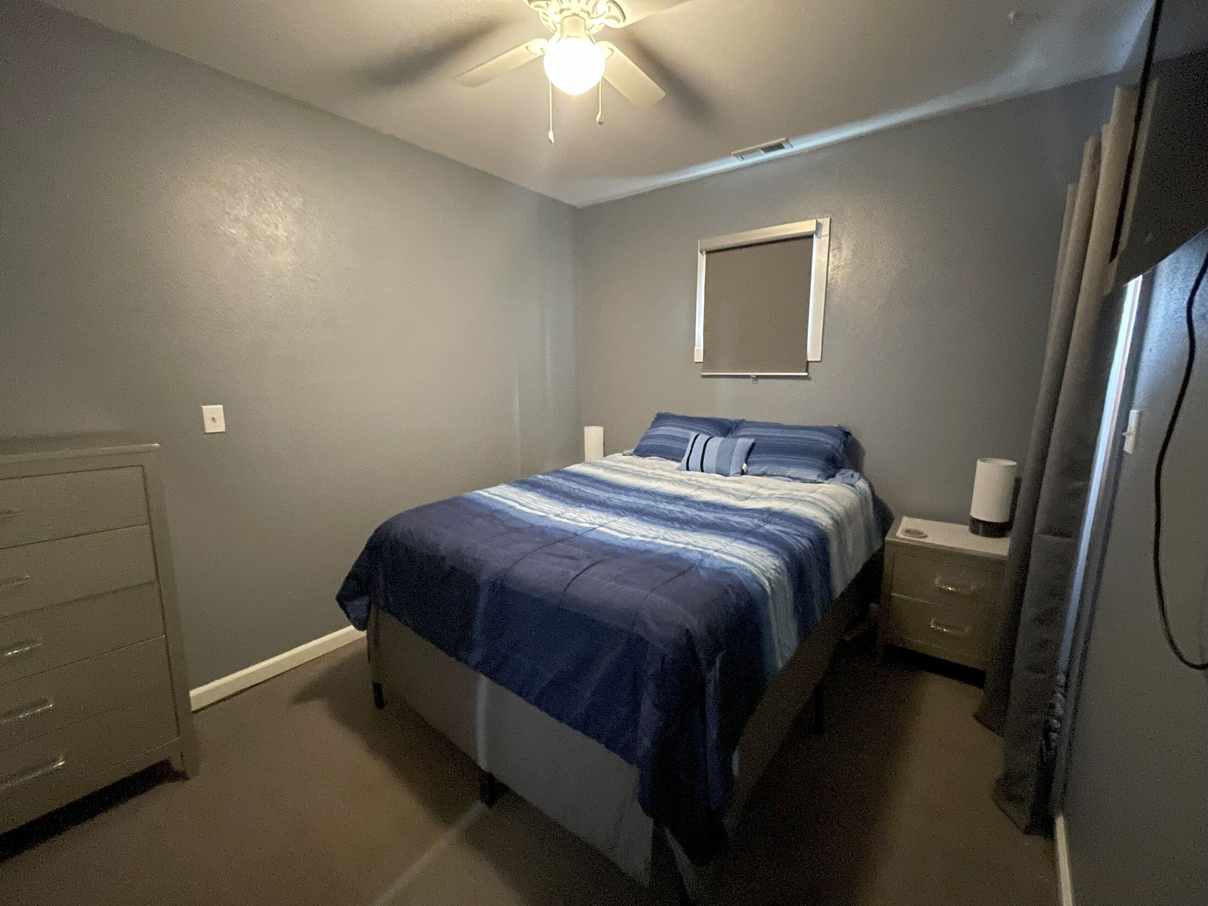 A bedroom with a bed, nightstands, a dresser, and a ceiling fan.