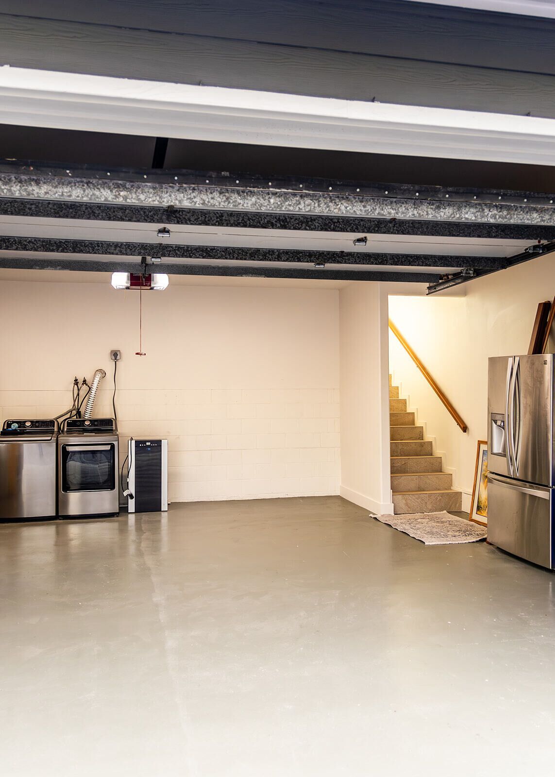 Ein geräumiger Kellerraum mit Betonboden, einem eingebauten Backofen, einem kompakten Kühlschrank und einer Treppe, die nach oben führt.