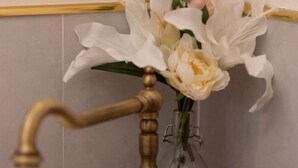 A bathroom with a white sink, a brass faucet, a vase with white and pink flowers, and a soap dispenser. - One Bedroom Apartment (Firenze)