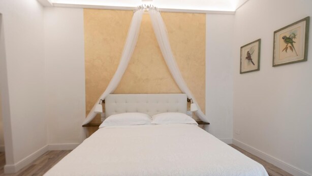 A bedroom with a large bed, white curtains, and two framed pictures on the wall. - One Bedroom Apartment (Firenze)