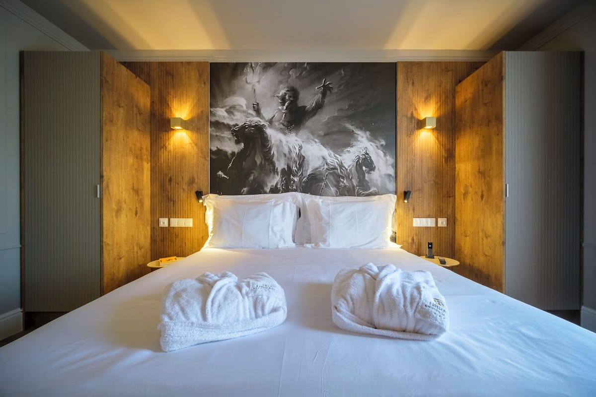 Une chambre d’hôtel avec un grand lit, deux serviettes blanches, un lambris en bois et un grand tableau accroché au mur.