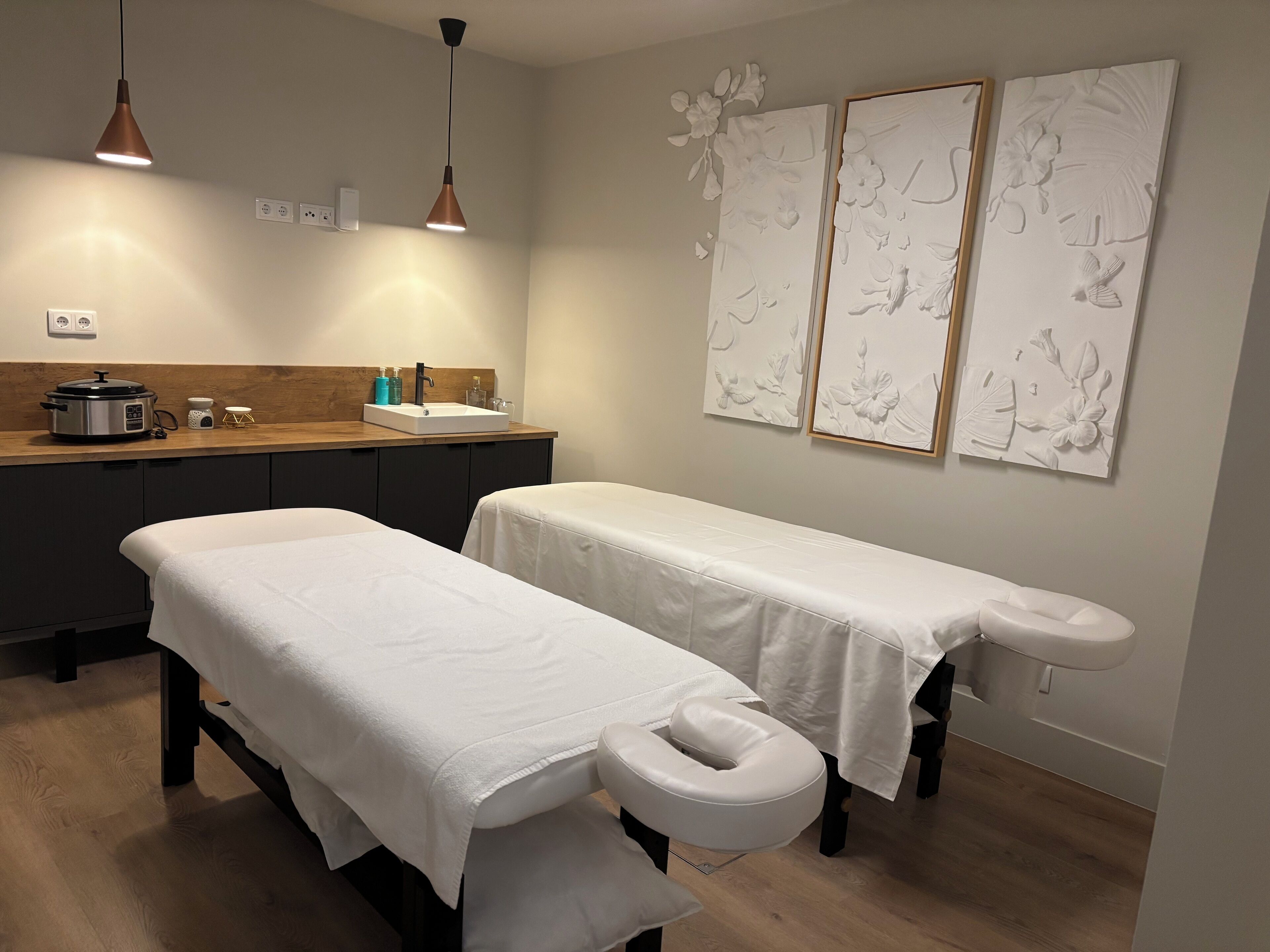A treatment room with a massage table, a foot bath, and a sink with a kettle.