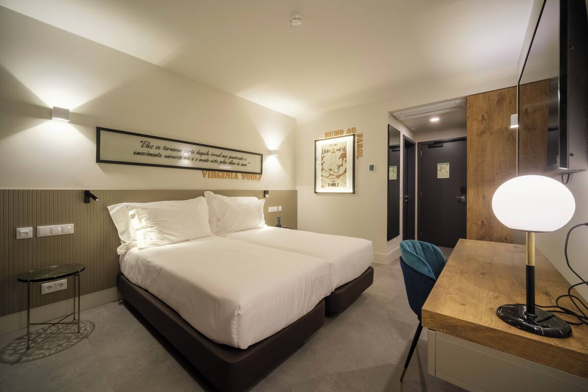 Une chambre d’hôtel avec un grand lit, des tables de chevet, un bureau avec une lampe et des œuvres d’art encadrées accrochées aux murs.