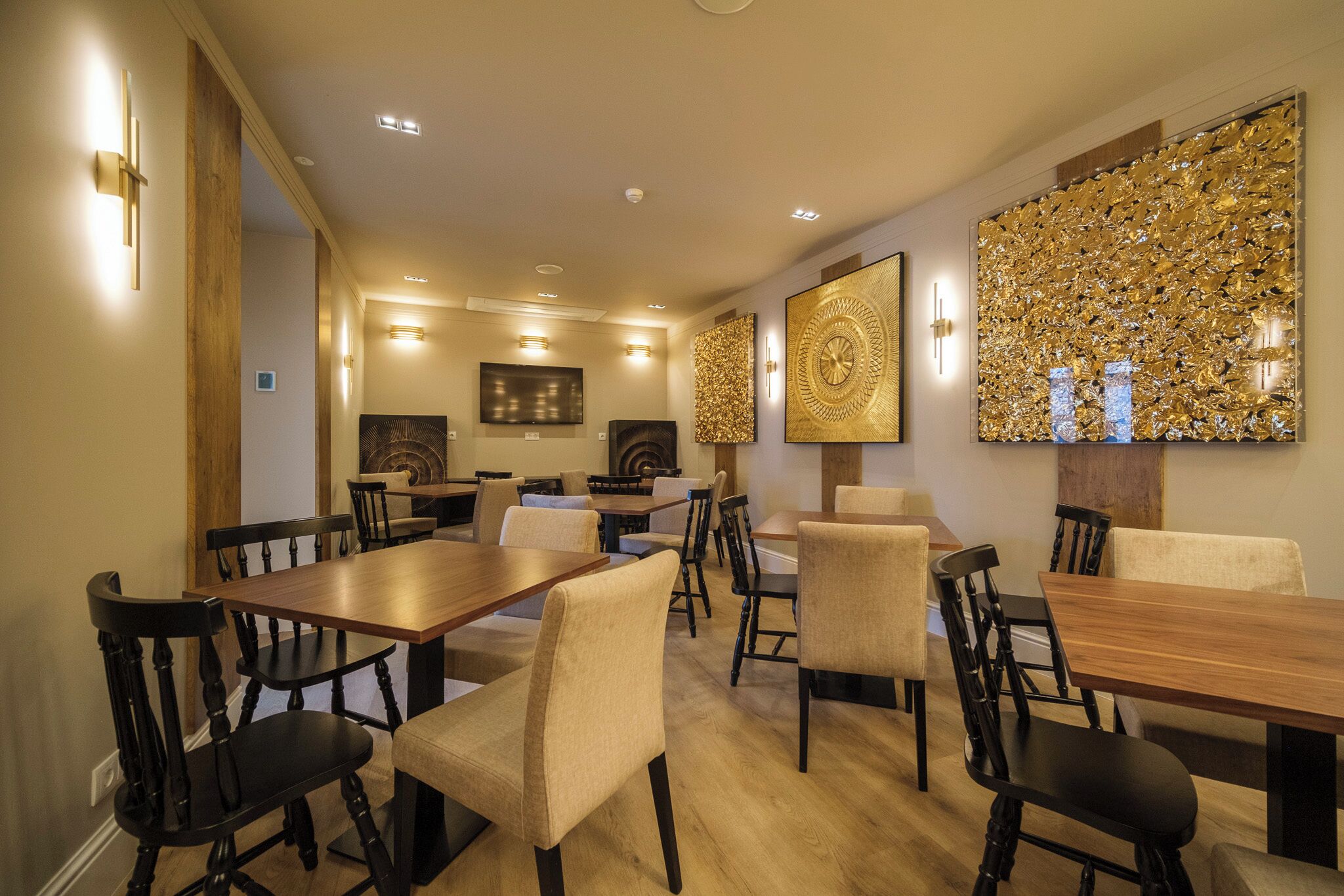 A dining area with wooden tables and chairs, a wall with decorative panels, and recessed ceiling lighting.