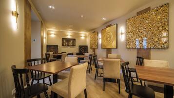 A dining area with wooden tables and chairs, a wall with decorative panels, and recessed ceiling lighting.
