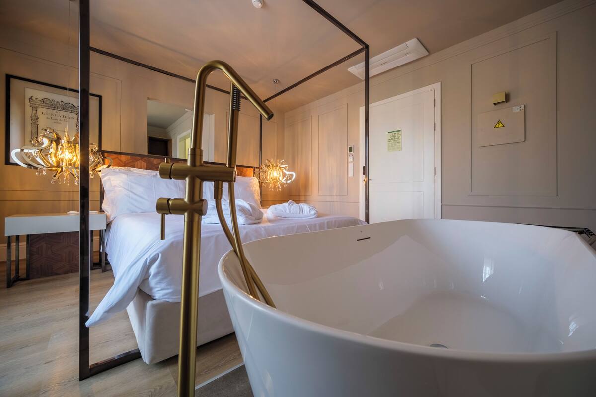 Une salle de bain moderne avec une grande baignoire blanche, un plancher en bois et un miroir orné d’un tableau.