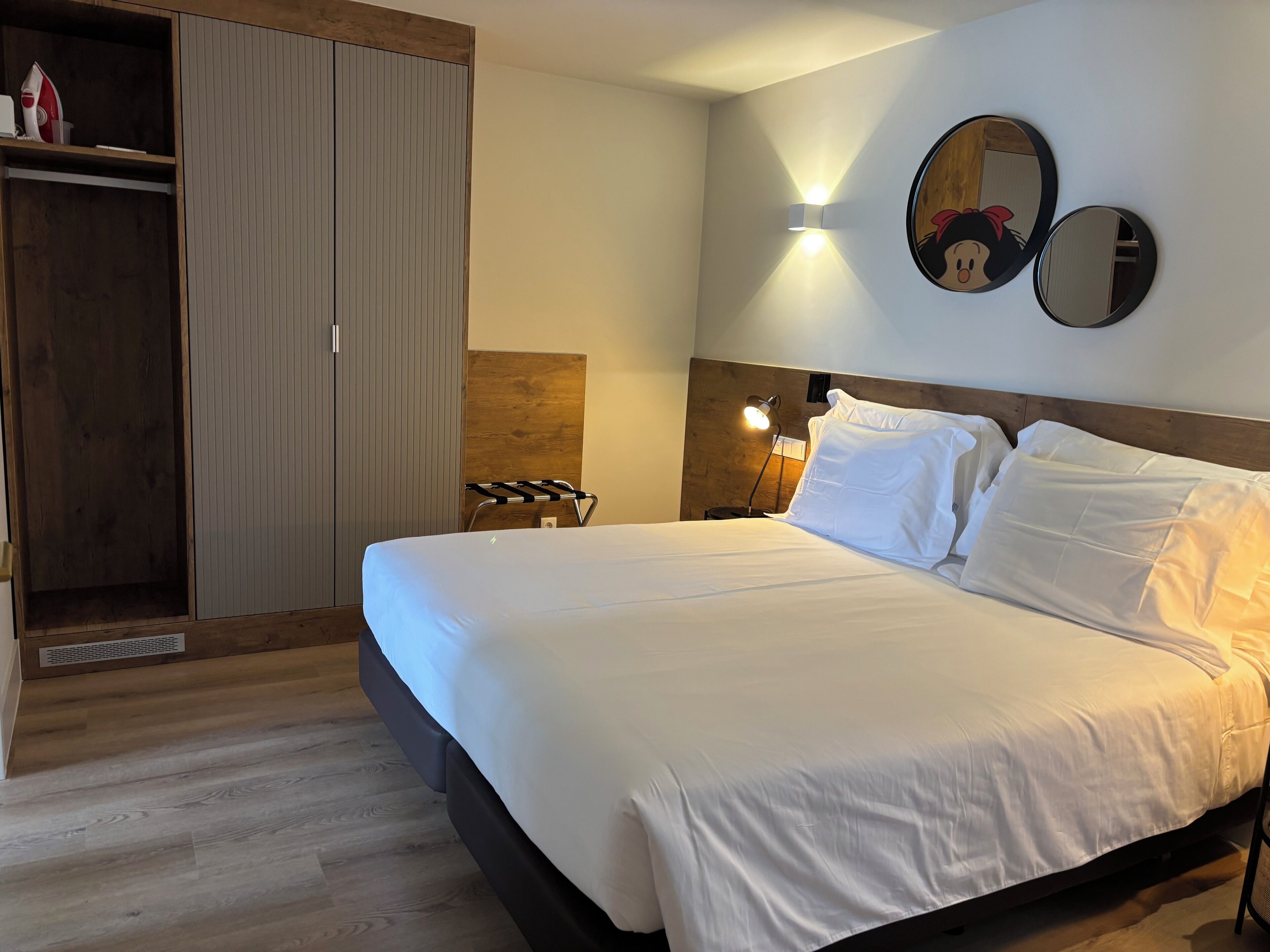 Cama bem arrumada com lençóis brancos, cabeceira de madeira e espelho fixado na parede.