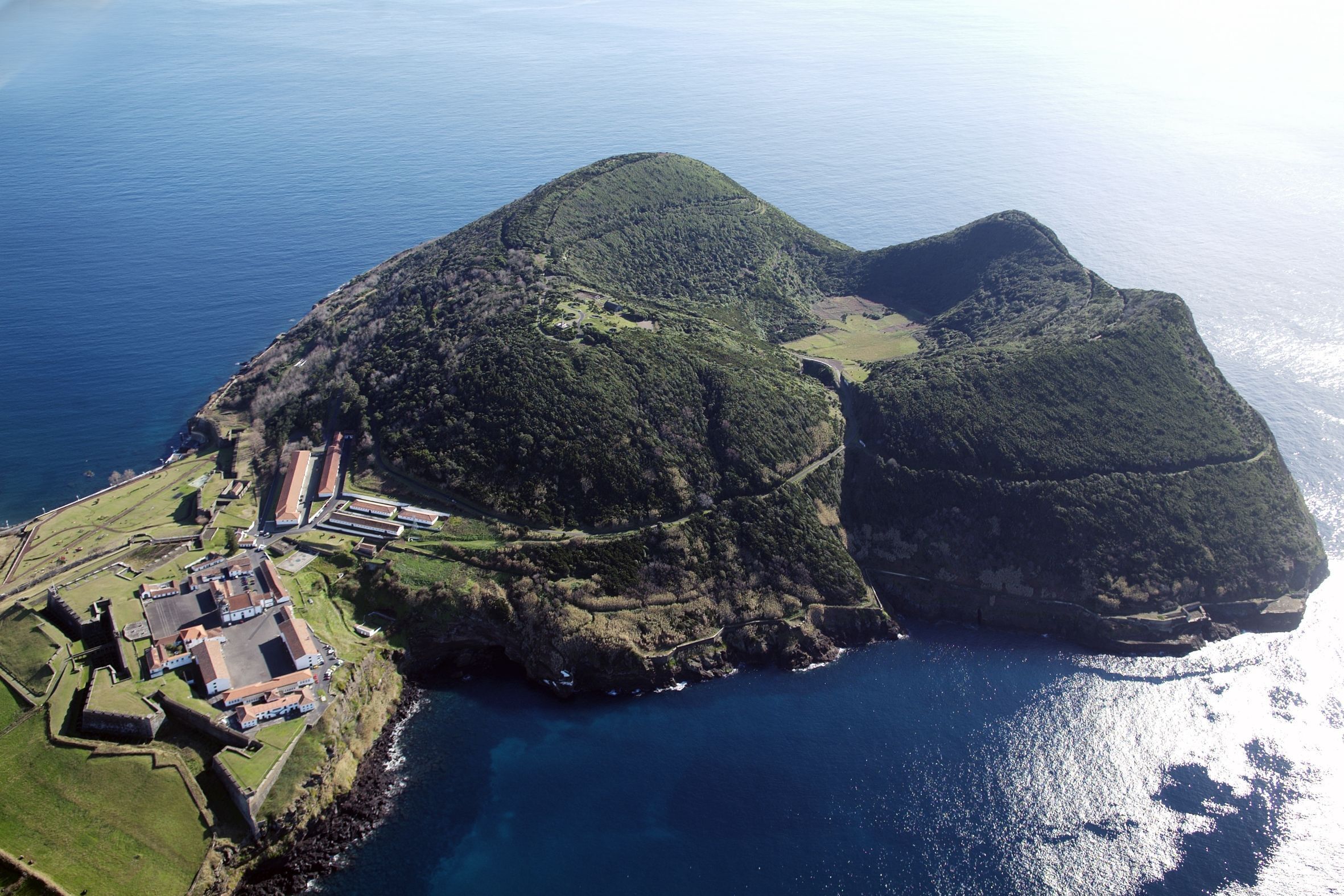 Vue aérienne d’une île côtière, avec une structure fortifiée et un petit village.
