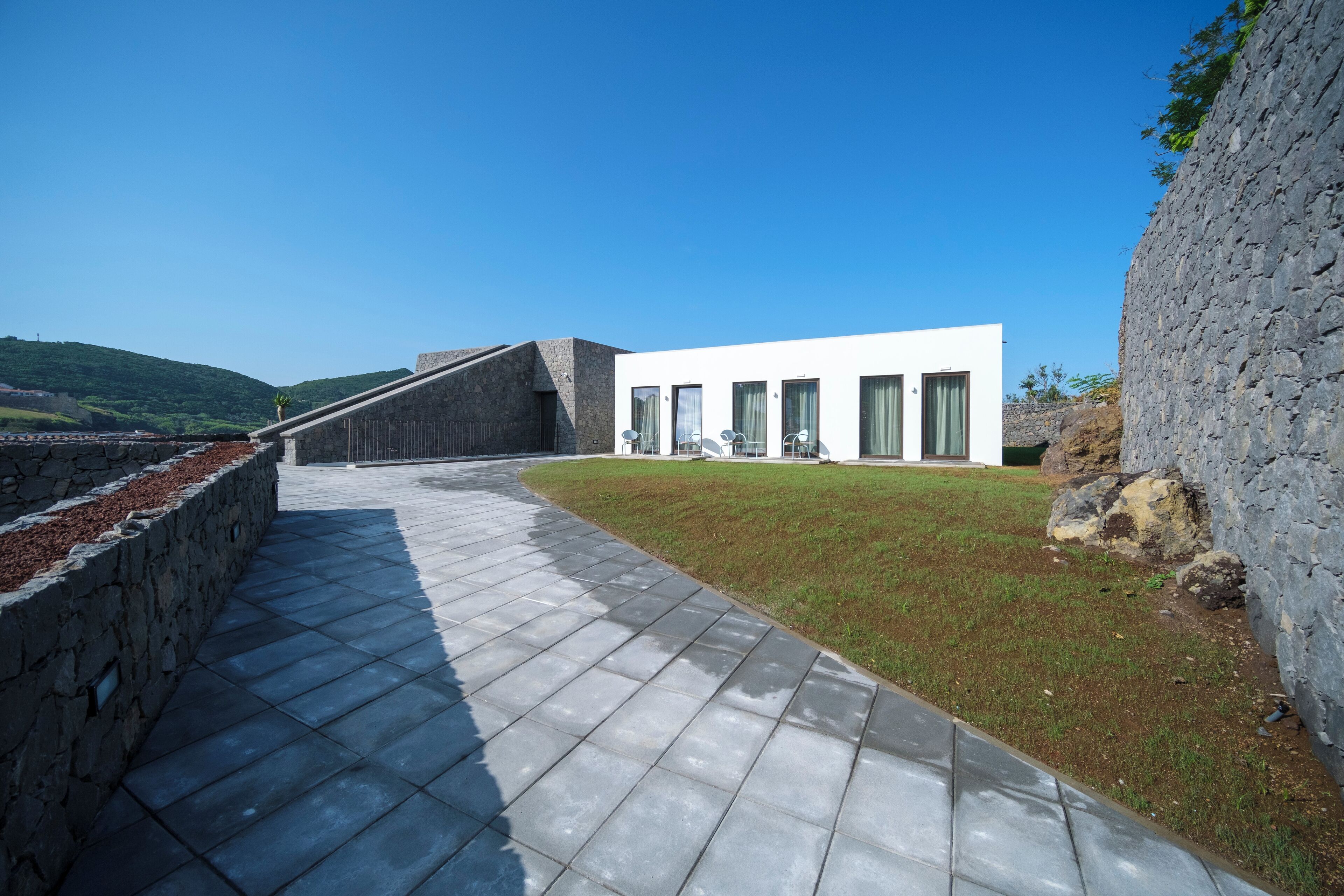 A modern building with a flat roof, a paved walkway, and a grassy area.