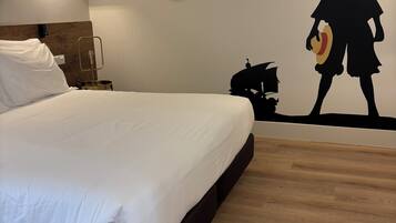 Uma cama bem arrumada com lençóis brancos, uma mesa de cabeceira com abajur, e uma parede com espelho circular e uma obra de arte em silhueta.