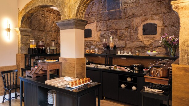 Een ontbijtbuffet met stenen bogen, een koffiehoek en diverse ontbijtartikelen.
