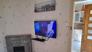 Une pièce avec un téléviseur fixé au mur, un sol à motifs, une porte et un petit meuble.