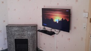 Un salon avec un téléviseur fixé au mur, une cheminée, des carreaux de sol à motifs et un tableau représentant un paysage urbain, placé au-dessus du téléviseur.