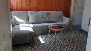 Une pièce avec un mur lambrissé en bois, un canapé gris, une petite table ronde sur laquelle se trouve un objet rouge et noir, et des carreaux de sol à motifs.