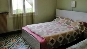 Une chambre à coucher avec un lit, une chaise, un radiateur et une fenêtre avec des rideaux.