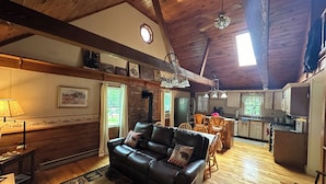 L’intérieur chaleureux d’un chalet avec un plafond en bois, un canapé en cuir, un coin repas et une cuisine.