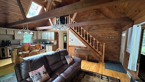 Une cabane en bois spacieuse, dotée d’un salon avec un canapé en cuir, une table à manger et une cuisine avec des meubles en bois et un four encastré.