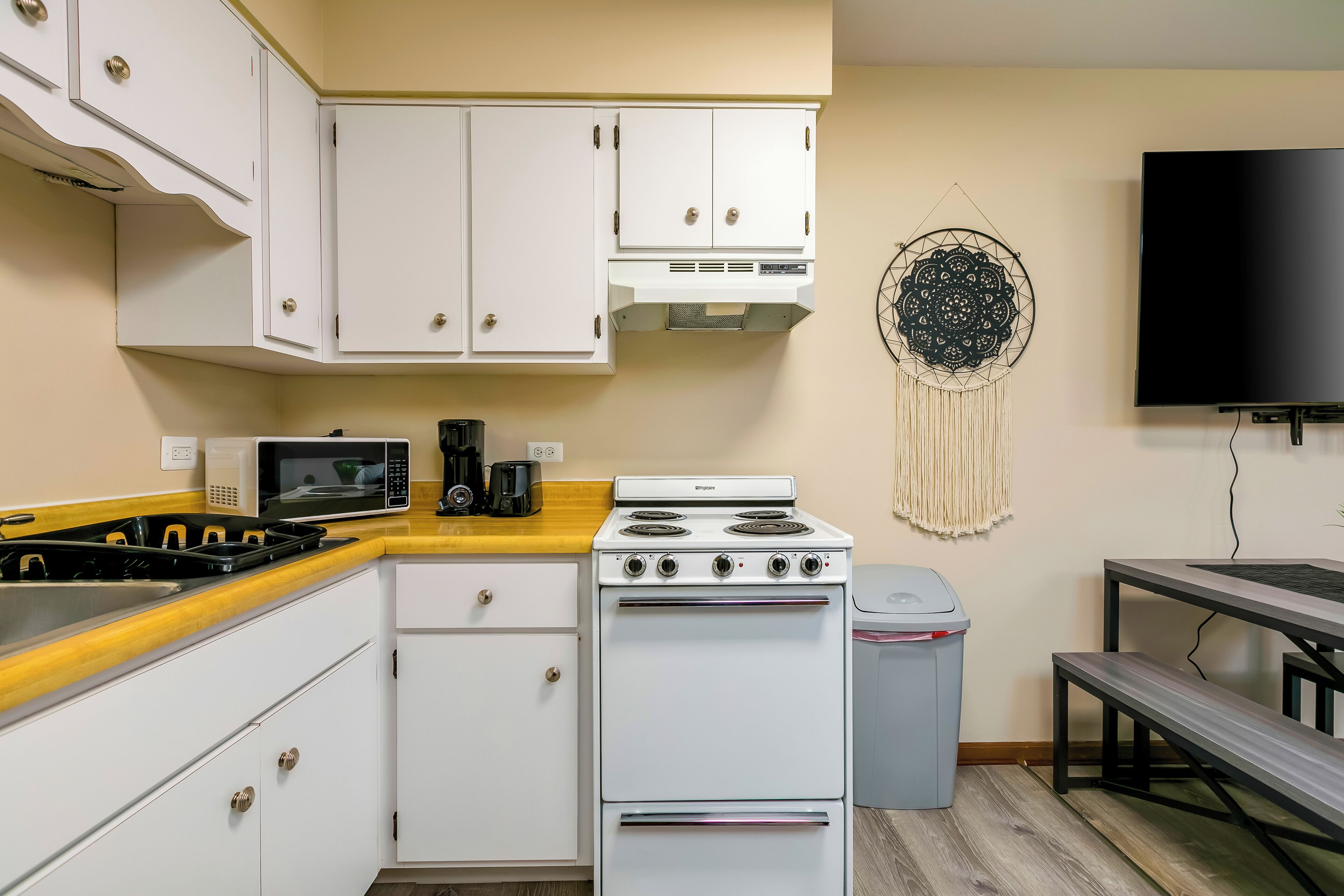 Une cuisine compacte avec des meubles blancs, une cuisinière, un four à micro-ondes et un attrape-rêves accroché au mur.
