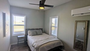 Ein Schlafzimmer mit Bett, zwei Fenstern, Deckenventilator und Klimaanlage.