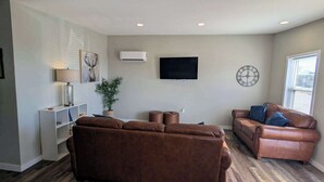 Ein Wohnzimmer mit braunem Ledersofa, einer braunen Lederliege, einem flachbildfernseher an der Wand und einer Topfpflanze.