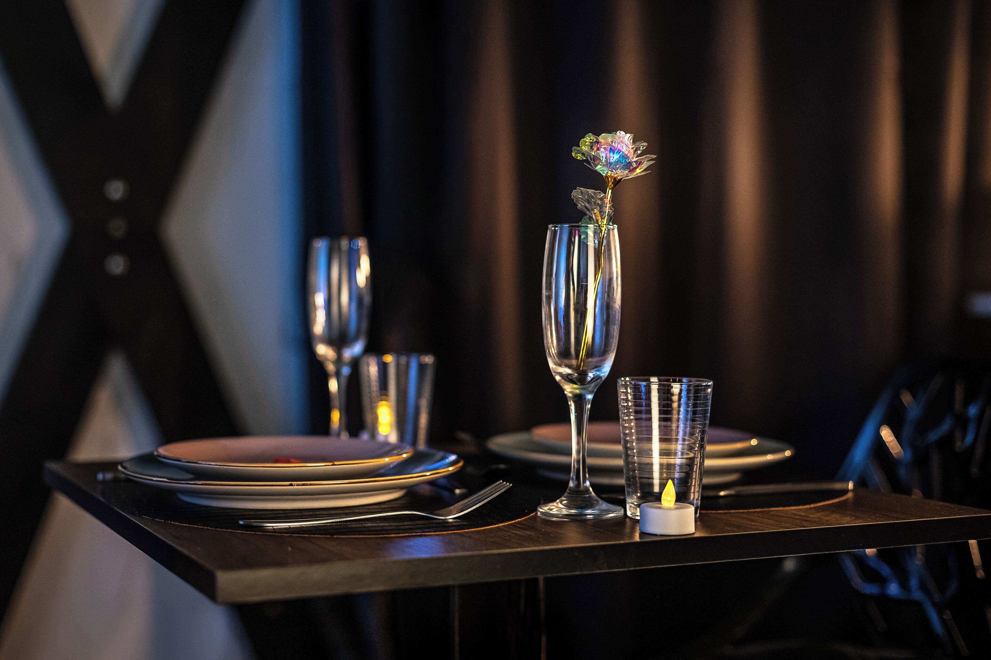 A table set with plates, cutlery, a candle, and a glass vase with a flower.