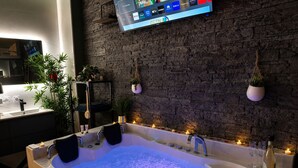 A modern bathroom with a large bathtub, a mounted TV, and decorative plants. - Secret Love Room Perpignan Full Équipé et Parking Privée (Perpignan)