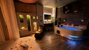 Ein Wellnessraum mit Massagesessel, Badewanne mit blauer Beleuchtung und einem Bett mit Rosenblüten.
