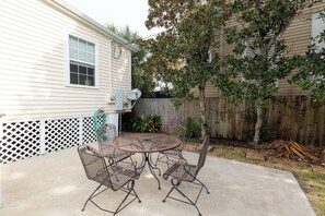 A patio with a round metal table and four chairs, a white fence, and a wooden fence in the background. - Historic Davidson-Penland House - Old Galveston Charm with Modern Amenities (Galveston)