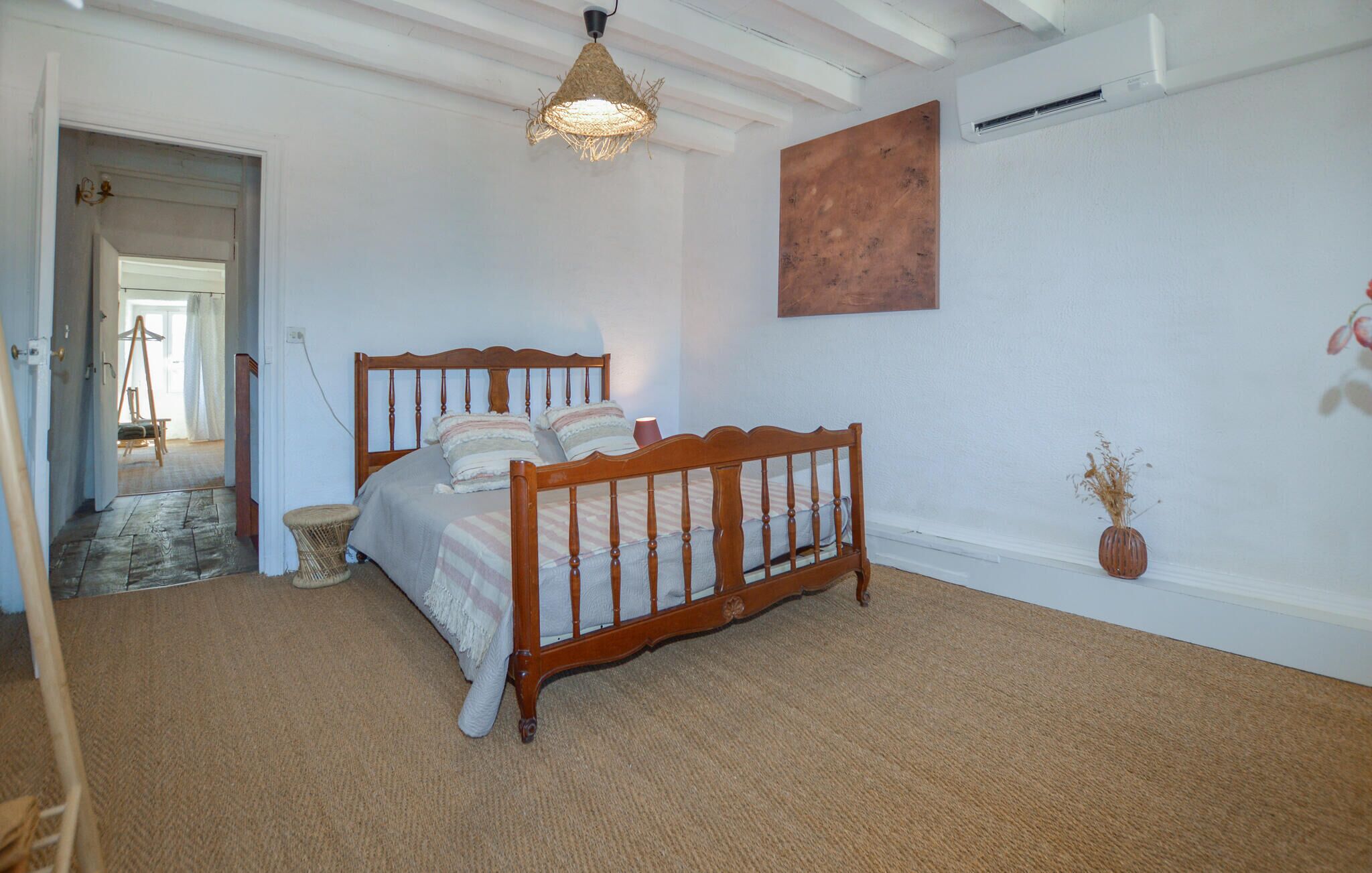 Une chambre avec un lit en bois, un luminaire suspendu, un tableau au mur et un petit vase contenant des plantes séchées.