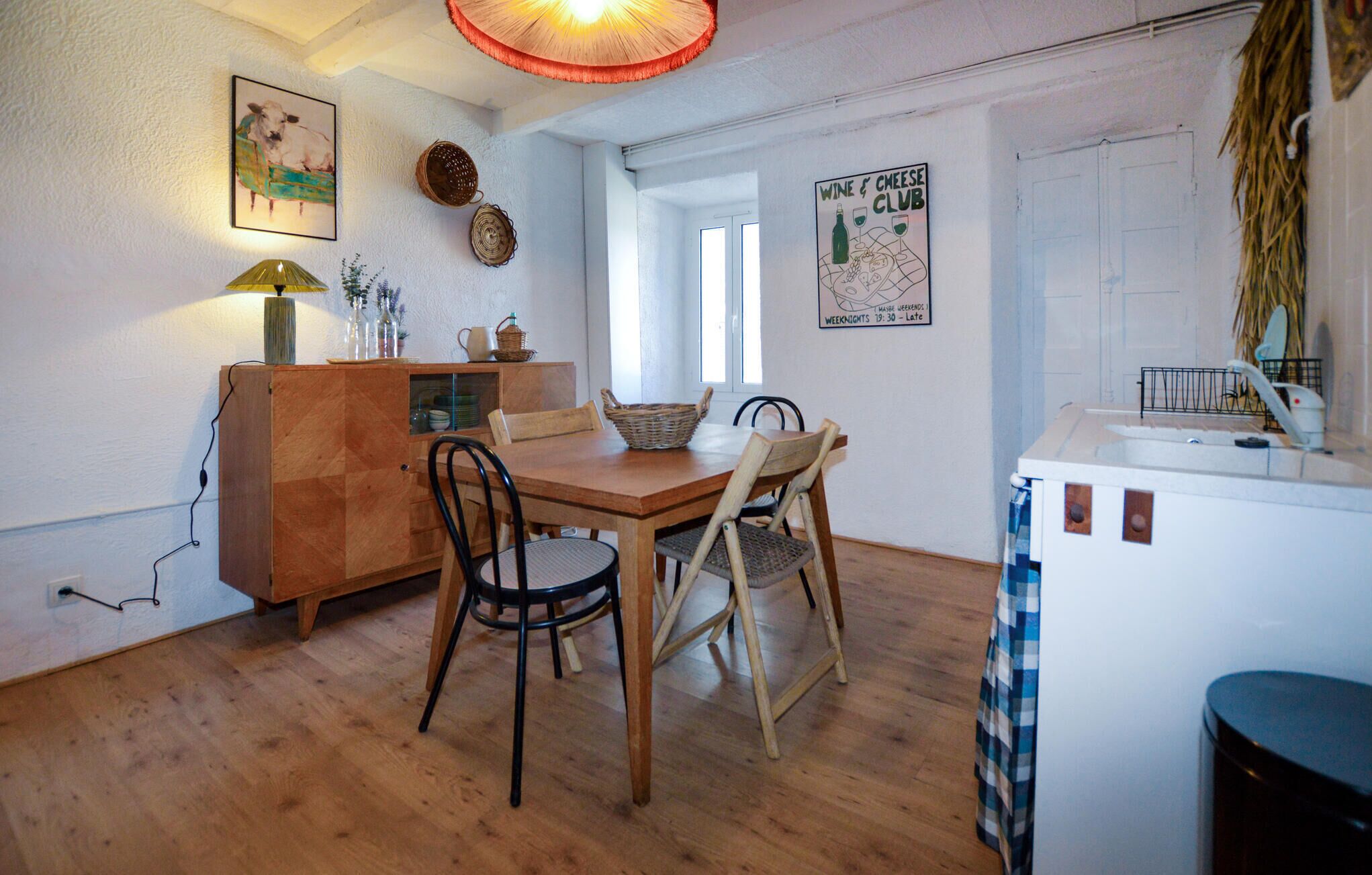 A dining area with a wooden table and chairs, a cabinet with a lamp, and a poster on the wall.