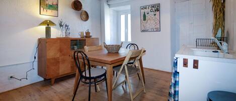 A dining area with a wooden table and chairs, a cabinet with a lamp, and a poster on the wall.