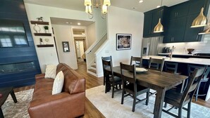 A modern living room with a brown leather sofa, wooden dining table, and dark cabinets.
