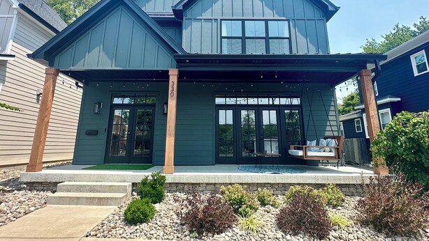 A modern two-story house with a front porch, a stone foundation, and a well-maintained garden.