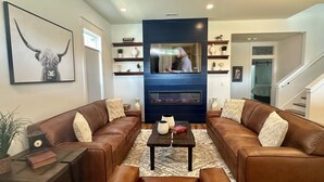 A living room with two brown leather sofas, a coffee table, and a fireplace. There are shelves with decorative items and a framed picture on the wall.