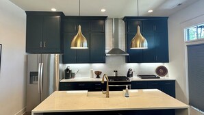 A modern kitchen with dark cabinets, stainless steel appliances, and pendant lighting.