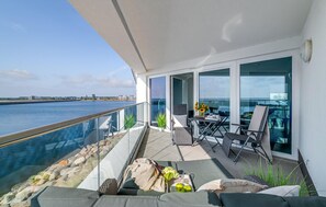 Un balcon avec vue sur l’eau, des sièges d’extérieur et une table sur laquelle sont posés divers objets.
