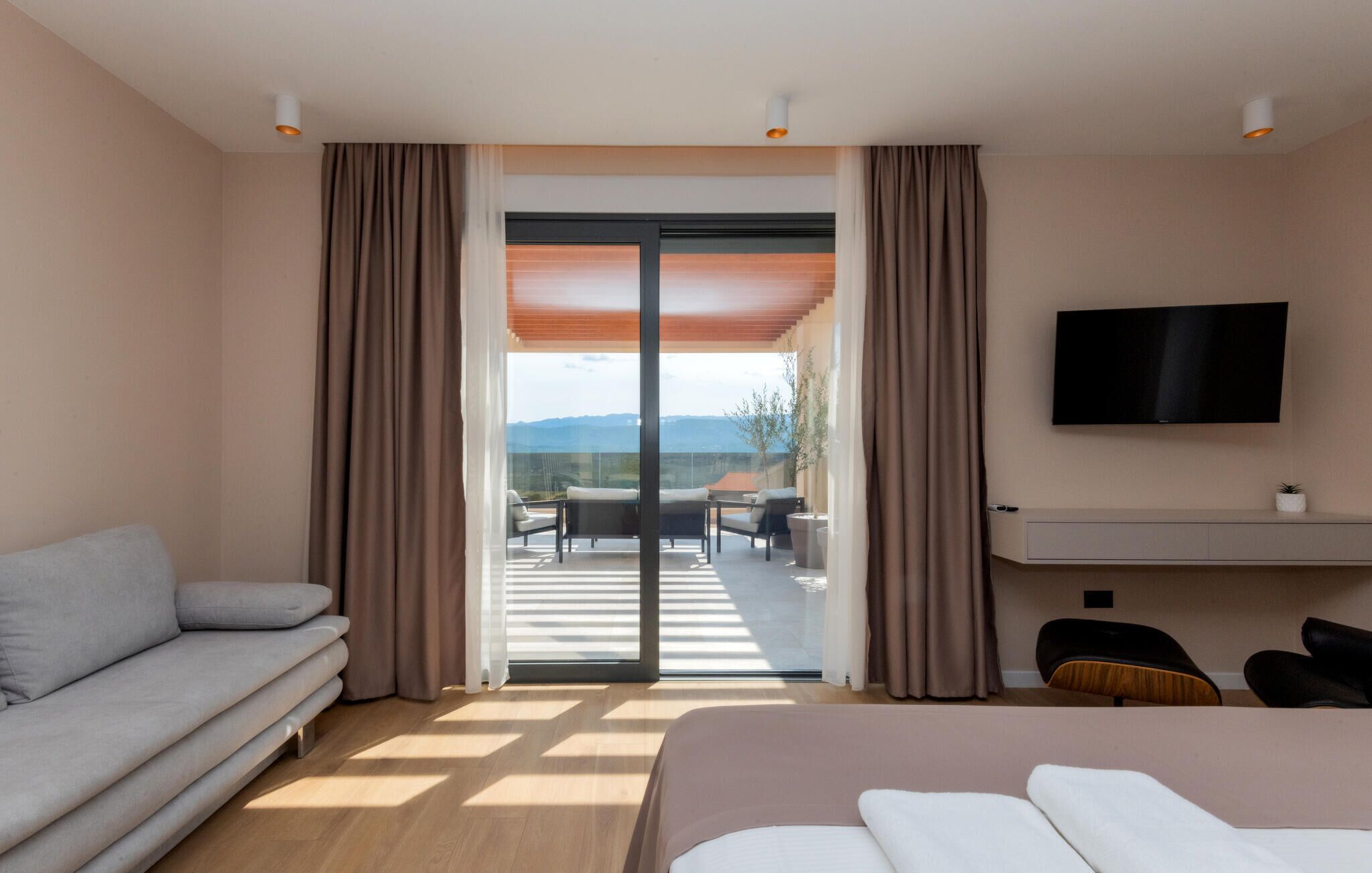 A hotel room with a bed, a sofa, a TV, and a balcony with a view.