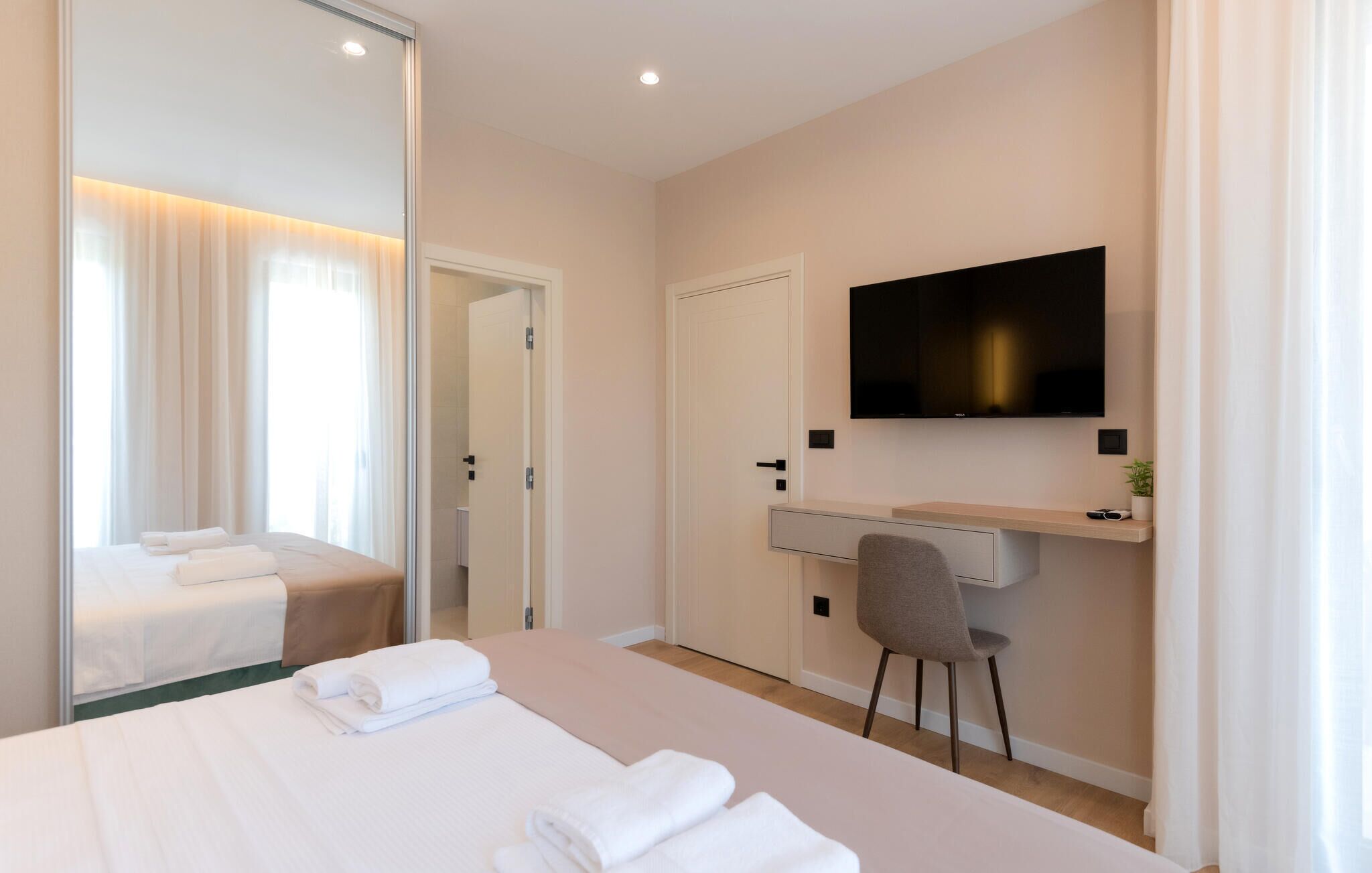 A modern hotel room with a large bed, a desk with a chair, a television mounted on the wall, and a sliding door leading to a bathroom.
