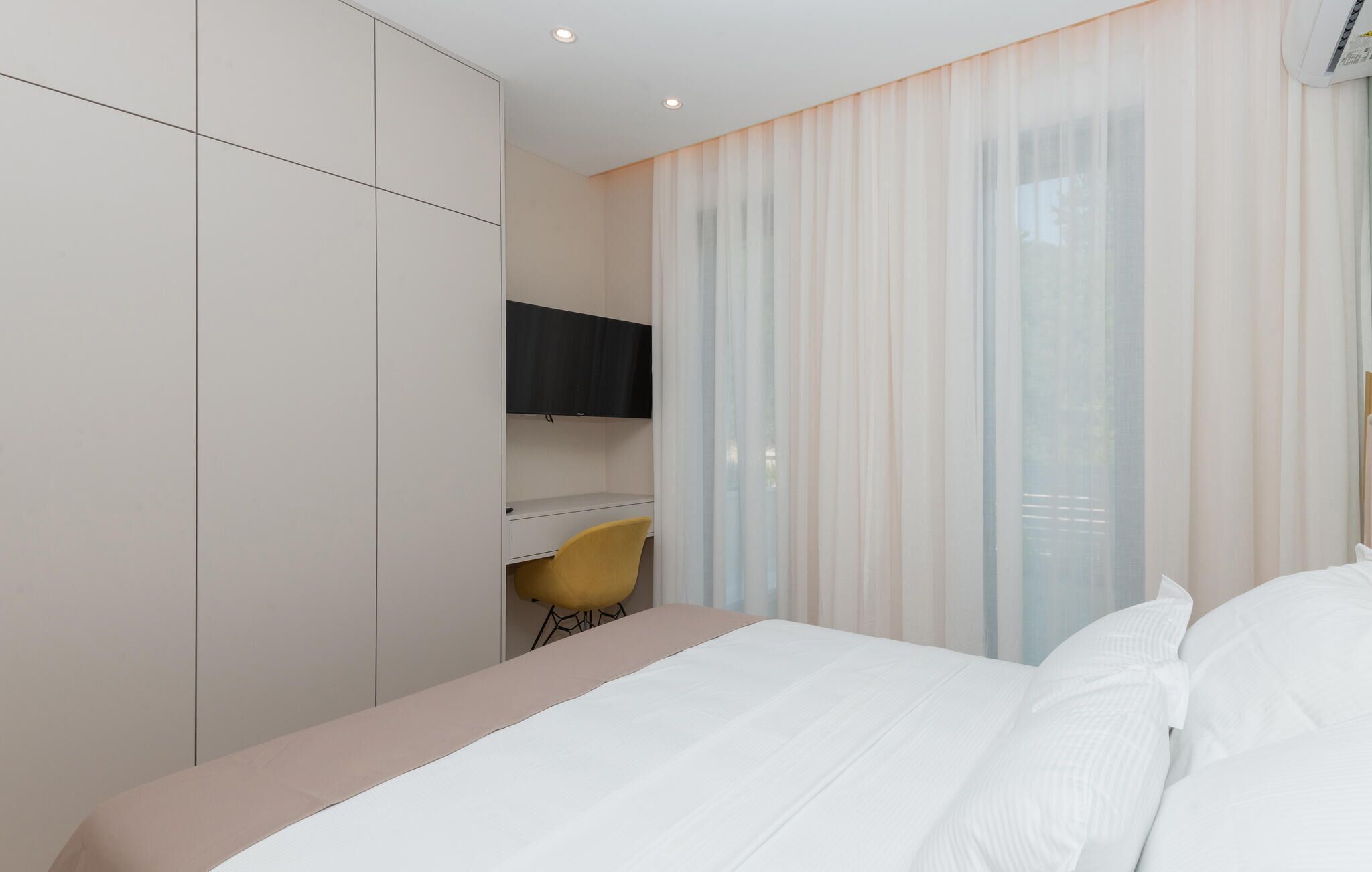Een hotelkamer met een bed, een bureau met stoel, een kledingkast en een televisie aan de muur.