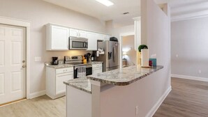 A modern kitchen with white cabinetry, a granite countertop, stainless steel appliances, and a small island. - Charming 3-bedroom house in Navarre -5 Mins from Beach. (Navarre)