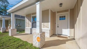A building with a covered porch, a door, and a brick pillar with a sign. - Charming 3-bedroom house in Navarre -5 Mins from Beach. (Navarre)